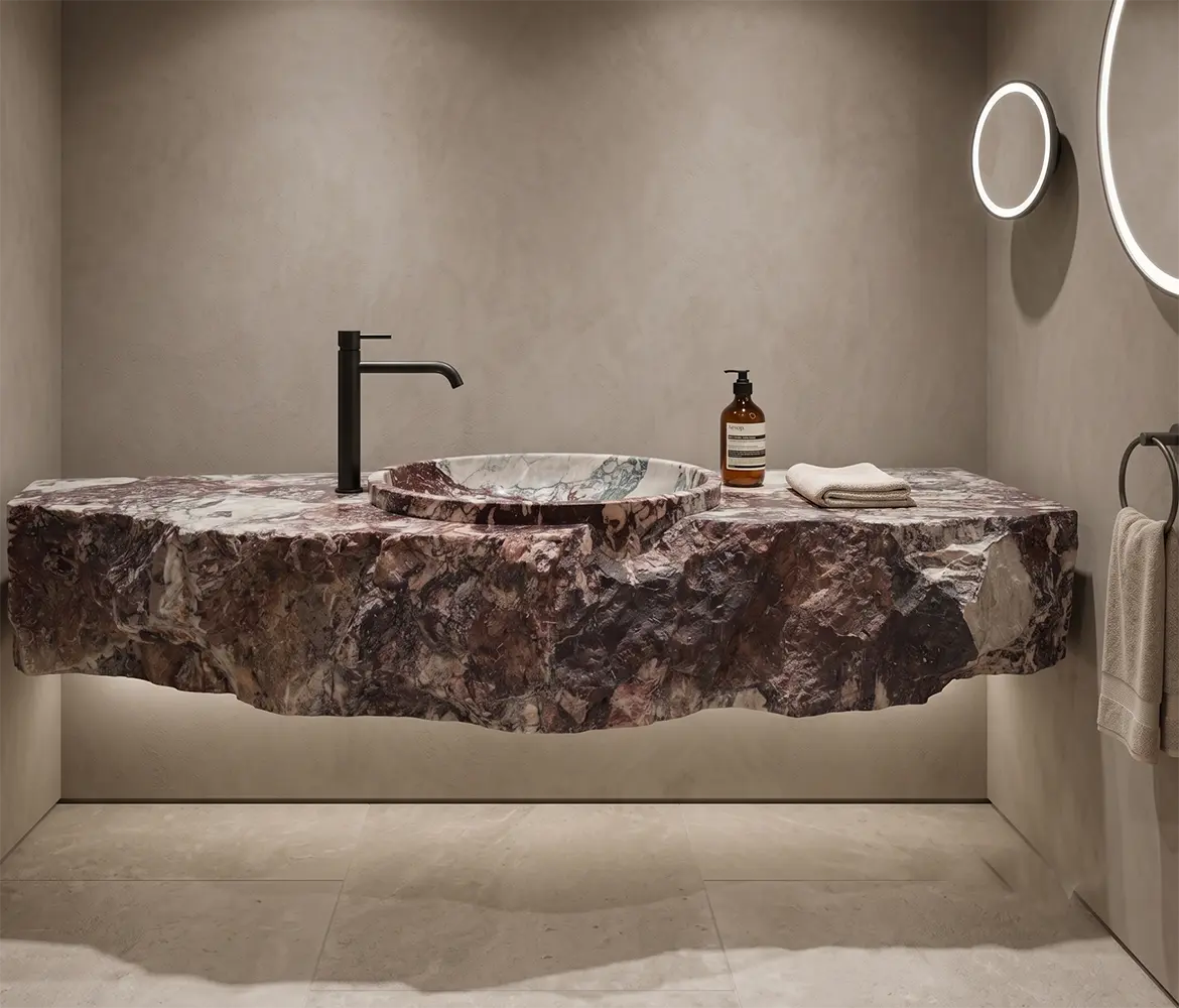 Raw Edge Marble Floating Sink Front view of a massive, wall-hung floating natural marble sink in a minimalist bathroom setting. The thick stone slab showcases deep burgundy, purple, and white veining. It features a polished top with a shallow integrated circular washbasin and a heavily chiseled, raw rock face front edge. The vanity is styled with a modern matte black faucet, an amber soap dispenser, and a folded towel, with under-sink LED ambient lighting casting a warm glow on the beige microcement walls.