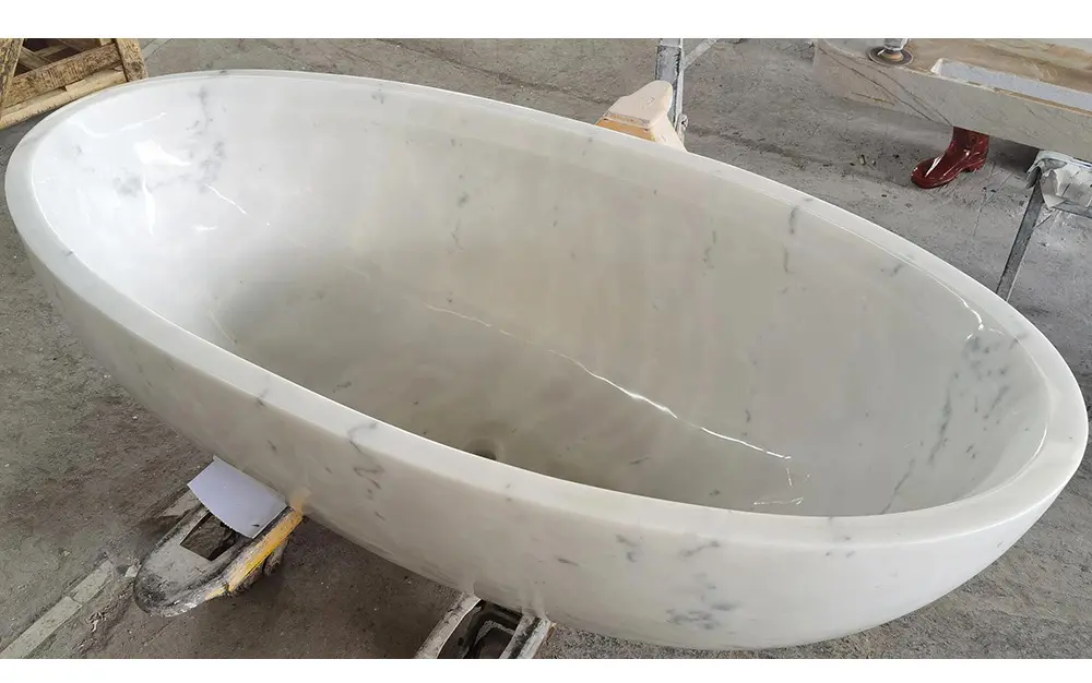 Luxury Solid White Marble Bathtub Custom Carved Caron Stone A newly carved, solid white marble freestanding oval bathtub sitting on a pallet jack inside the Caron Stone manufacturing facility.