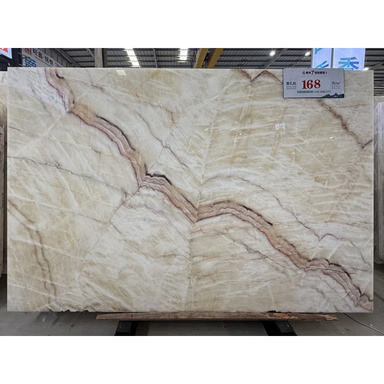Full jumbo slab of polished Rainbow Onyx showcasing a translucent ivory base with diagonal sweeping bands of red and burgundy veining, supplied by Caron Stone.