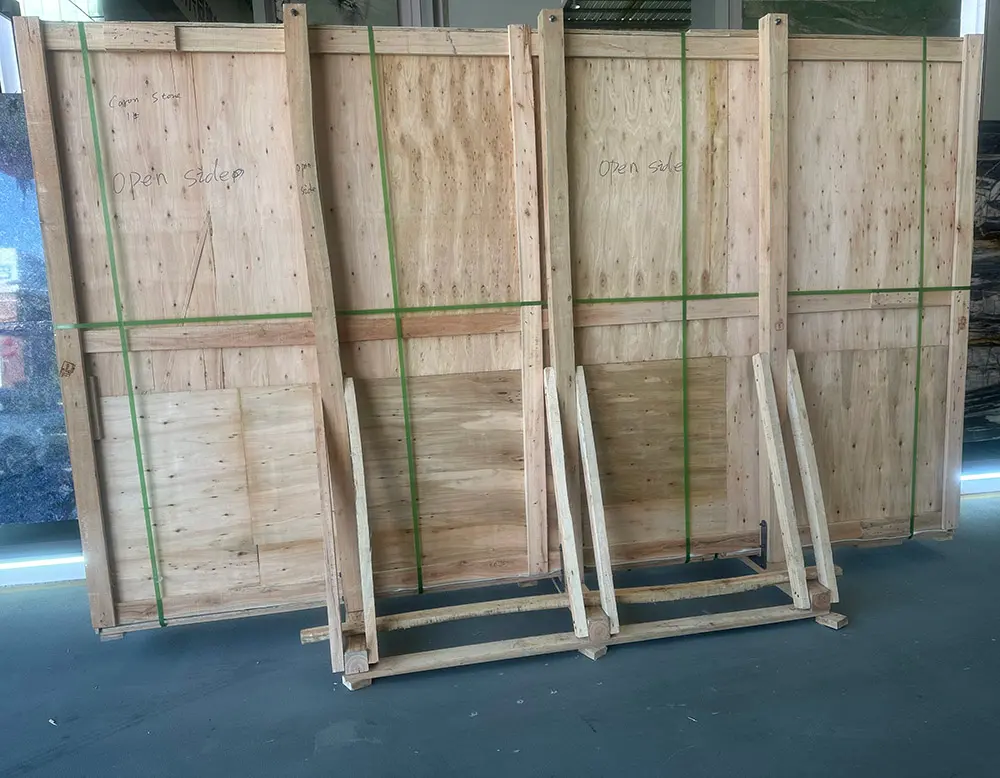 Large heavy-duty wooden A-frame crate secured with green high-tensile strapping, clearly labeled Caron Stone, used for packing and protecting stone slabs in a warehouse facility.