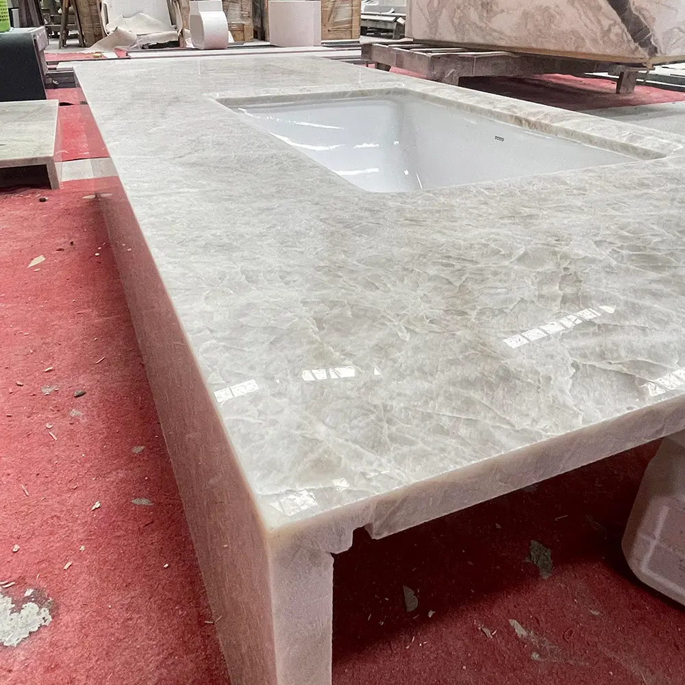 Taj Mahal Quartzite Precision Mitered Vanity Top Assembly Close-up perspective of a highly polished Taj Mahal Quartzite bathroom vanity top with a deep vertical mitered apron edge and white undermount sink, staged on a red floor inside a stone fabrication plant.