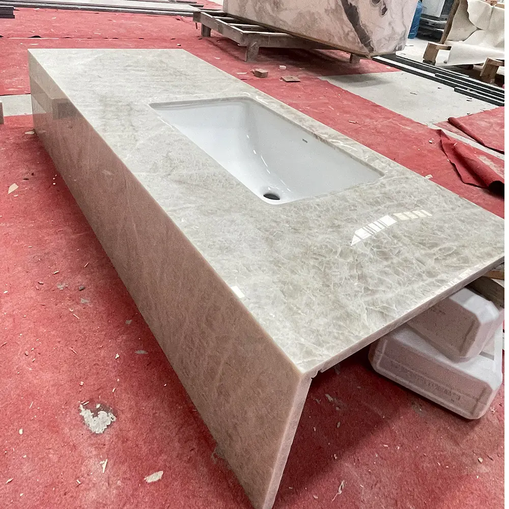 Taj Mahal Quartzite Extended Vanity Top with Deep Mitered Apron Long polished Taj Mahal Quartzite vanity top with a white undermount sink and a deep vertical mitered apron edge, resting on a red protective mat in a stone fabrication factory.