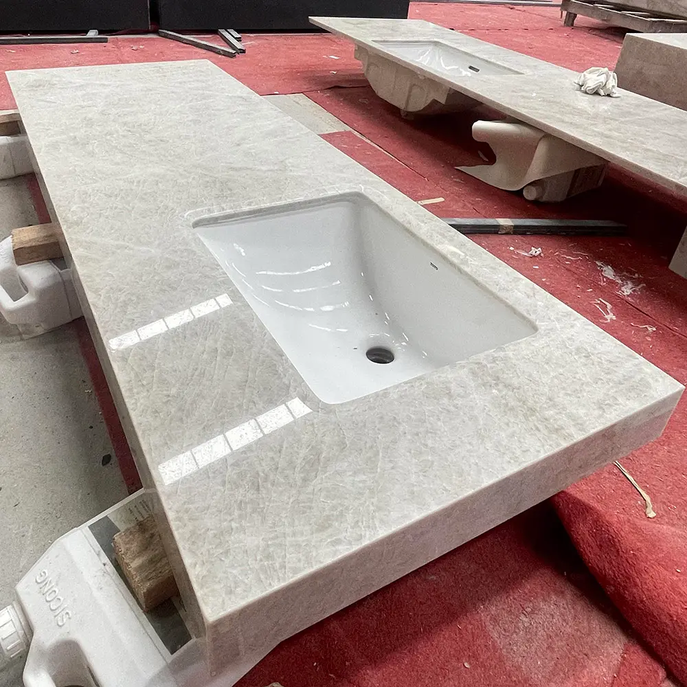 Taj Mahal Quartzite Pre-Assembled Vanity Top with Undermount Sink Polished Taj Mahal Quartzite bathroom vanity top with an attached white ceramic undermount sink and thick mitered edges, resting on protective red flooring inside an industrial stone manufacturing facility.