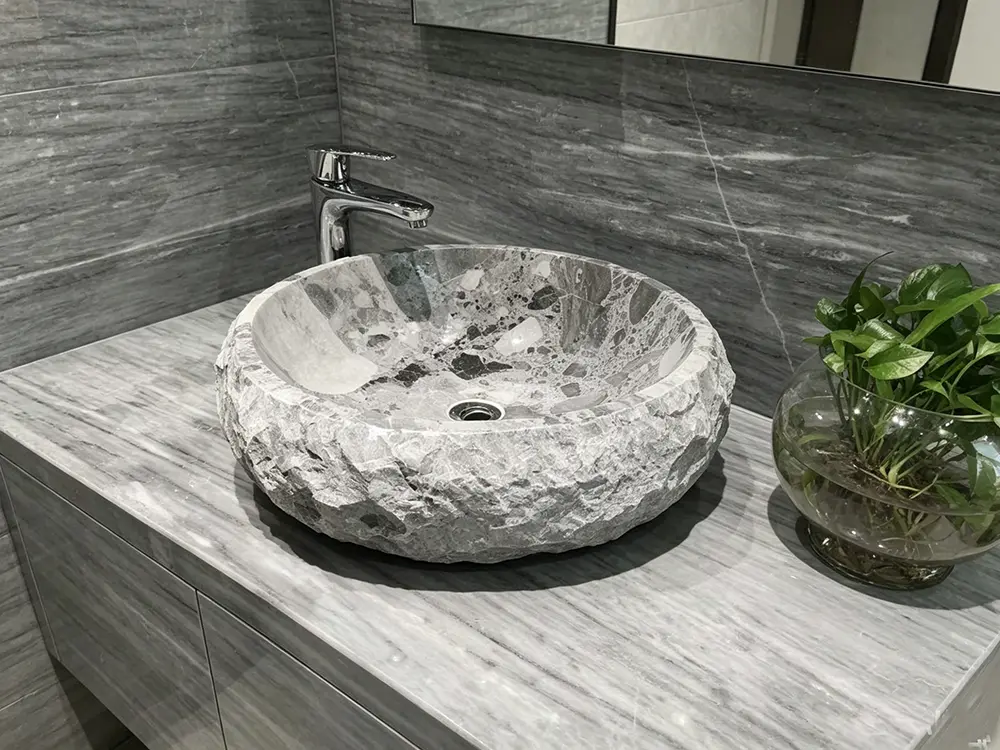 The Art of Carving Bespoke Stone Sinks Caron Stone artisan using specialized tools to hand-chisel the exterior of a CNC-milled Ceppo Noir marble vessel sink.