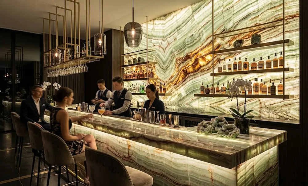 Luxury Commercial Bar with Backlit Green Onyx Custom luxury commercial bar counter featuring a glowing, backlit Green Onyx front fascia and polished top.