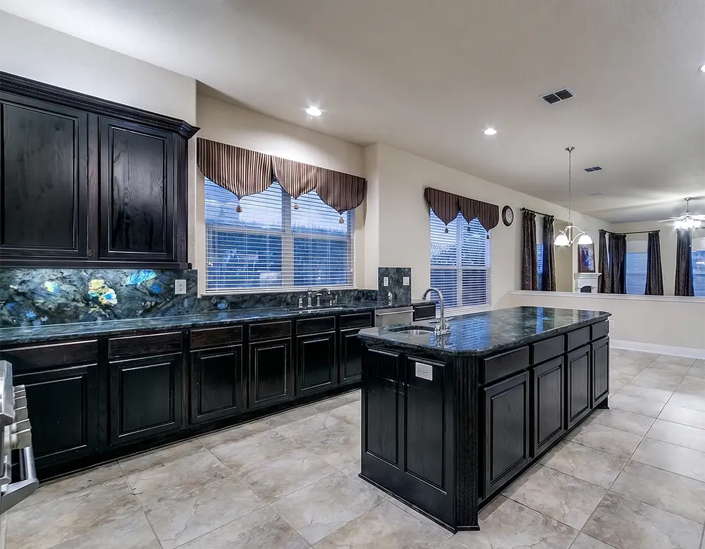 Continuous Labradorite Full-Height Backsplash A dark grey Labradorite Blue granite countertop extending up the wall to form a continuous, dramatic full-height kitchen backsplash.