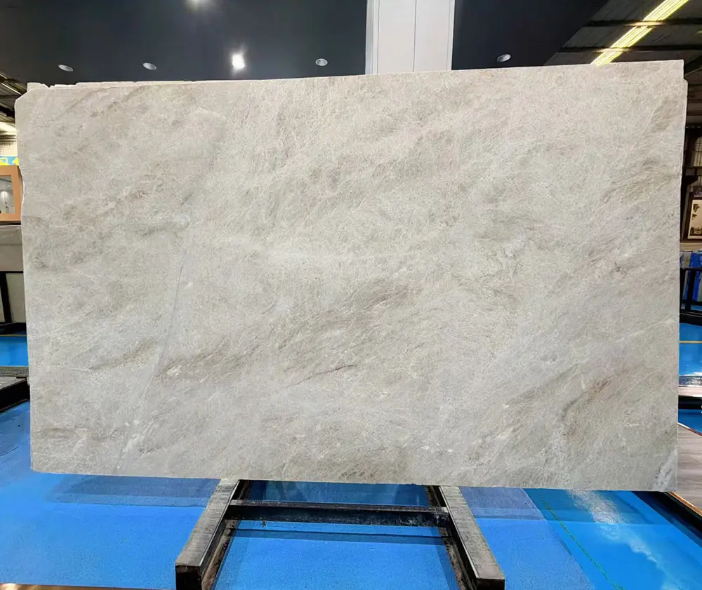 premium-taj-mahal-quartzite-jumbo-slab-caron-stone Large premium Taj Mahal Quartzite jumbo slab with natural light beige and grey veining resting on a steel A-frame in an industrial manufacturing facility.