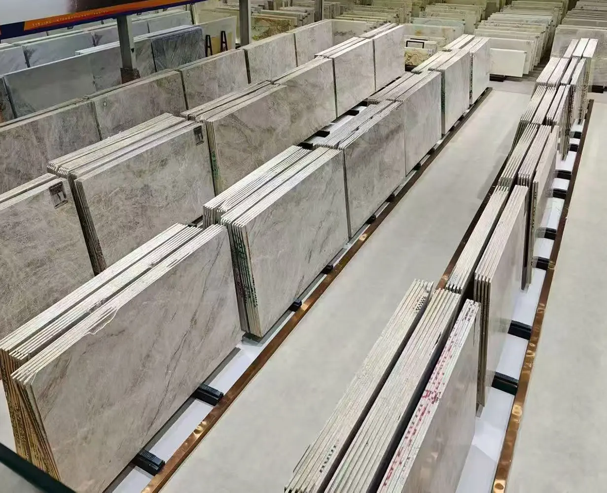 taj-mahal-quartzite-slab-factory High-angle warehouse view of an industrial stone factory showcasing multiple rows of precisely organized Taj Mahal Quartzite slabs in metal A-frame display racks.